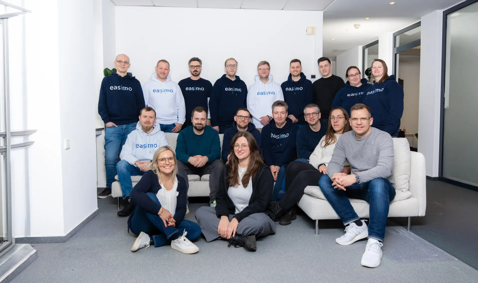 Rund 20 Mitarbeitende von easimo sitzen und stehen gemeinsam im Büro für ein Teamfoto.