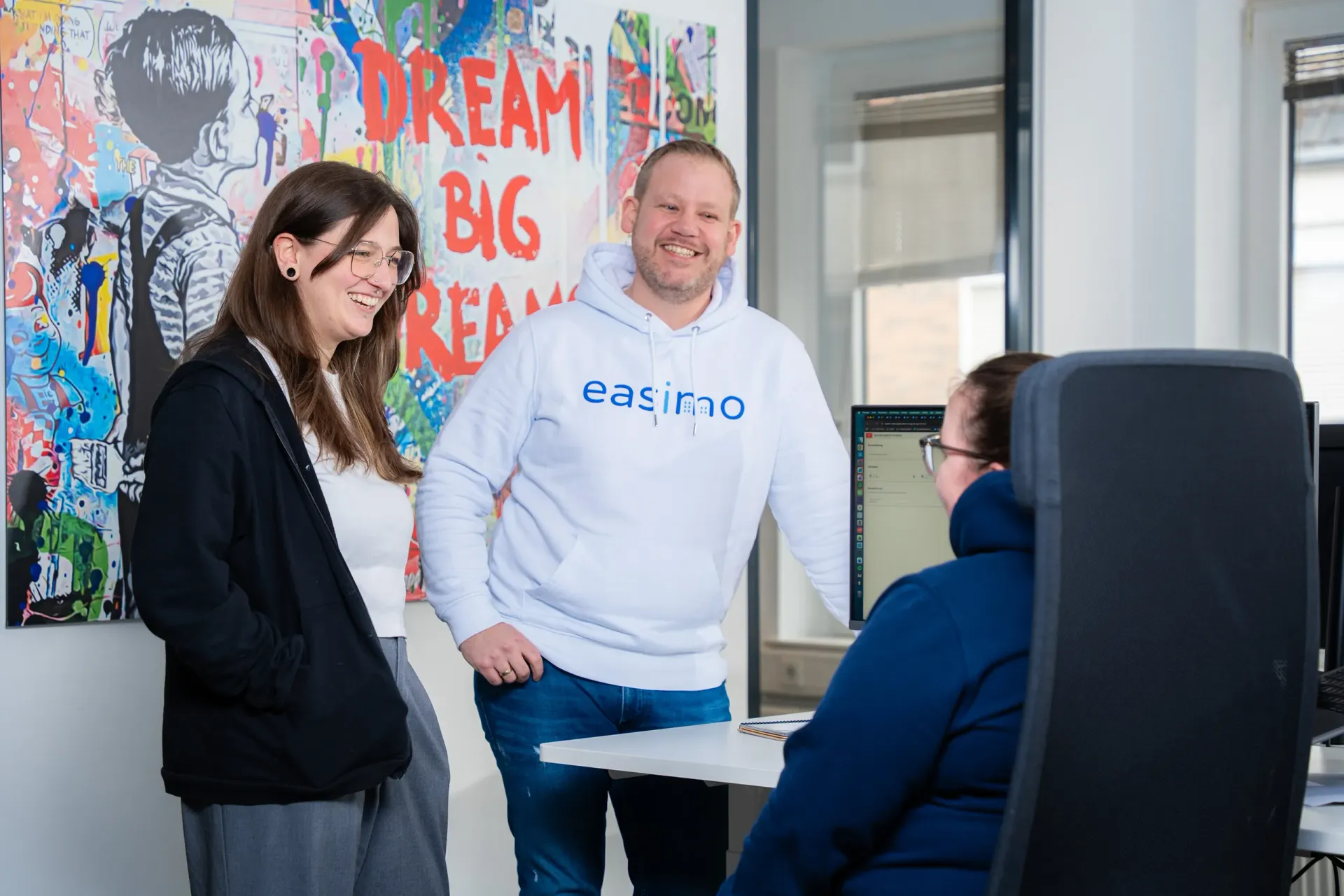 Consulting-Team von easimo im Gespräch im Büro: Mitarbeitende beraten sich an einem Arbeitsplatz zur webbasierten Immobilienverwaltungssoftware.